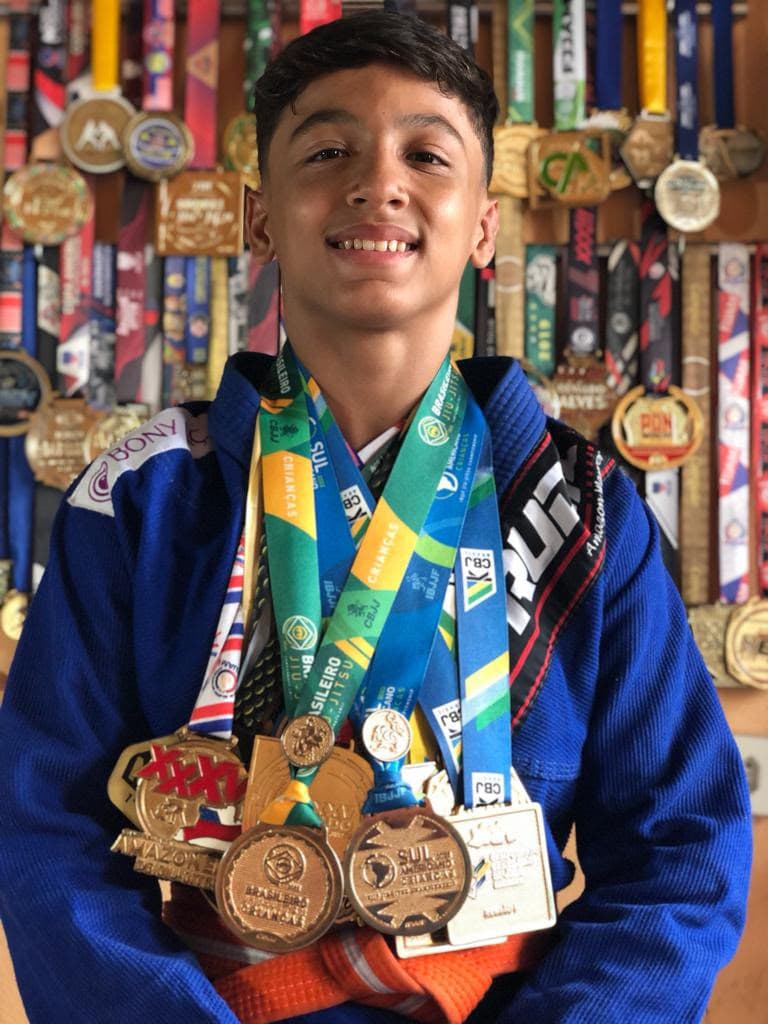 Isaque com várias medalhas no peito e outras medalhas ao fundo